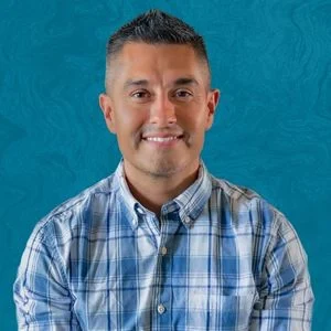 Justin Pearce Smiling In Front Of Blue Background